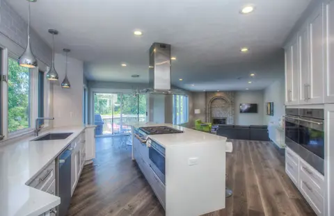 Modern kitchen with white shaker cabinetry, large white island with waterfall edge, stainless steel appliances, wood plank