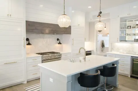 Bright white kitchen with shaker-style cabinetry, white quartz island with waterfall edge, black task chairs, stainless