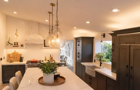 Modern kitchen featuring dark wood cabinetry, white quartz countertops, brass pendant lights, white range hood, and bar