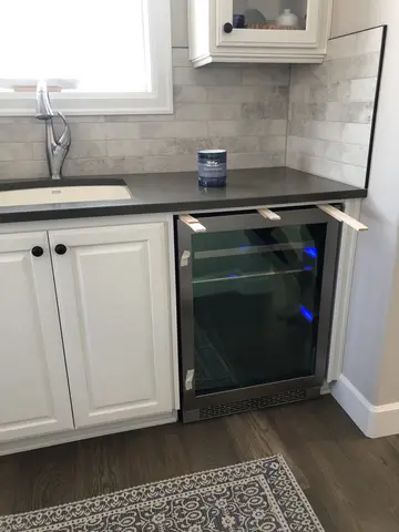 White shaker-style kitchen cabinets with dark countertop, gray subway tile backsplash, and stainless steel beverage cooler