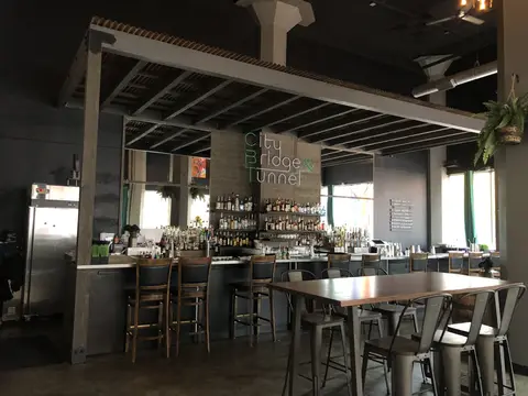 Modern bar restaurant interior with stainless steel service counter, wooden bar stools, exposed beam ceiling, and full