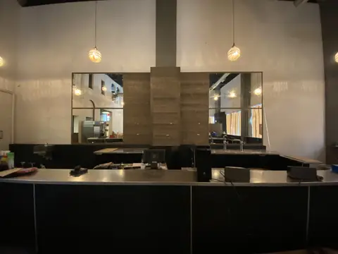 Modern commercial kitchen counter with black cabinetry, mirror backsplash panels, and suspended pendant lights above.