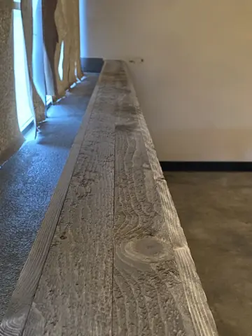 Long hallway with wood-look plank flooring, bright natural light from left-side windows, white walls and black baseboard