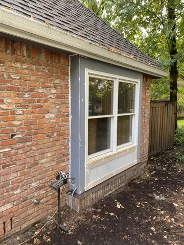 White-trimmed double-hung window installed on red brick exterior wall with blue-gray siding accent band and foundation