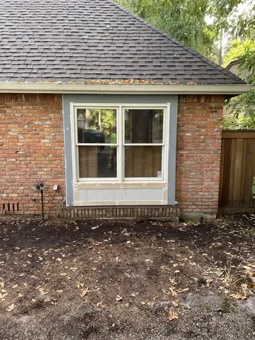 Brick house exterior with new white casement window, white trim surround, and gravel landscaping.