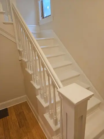 White painted interior staircase with spindle balustrade descending to wooden flooring, natural light from upper window.