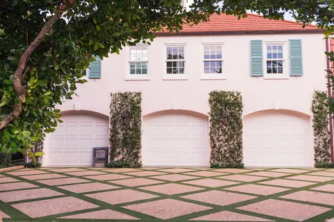 Three-car garage with pink stucco walls, white panel doors, climbing ivy on columns, and geometric diamond pattern concrete