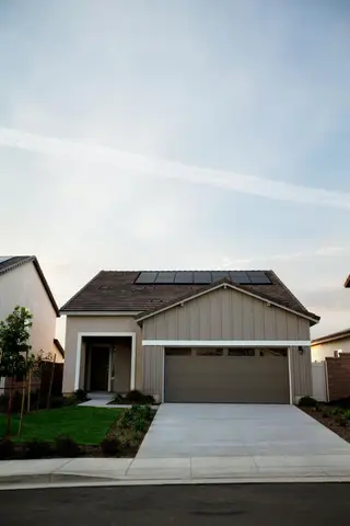Modern gray-sided single-story home with dark pitched roof, two-car garage, concrete driveway, and front landscaping.