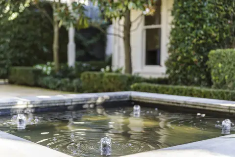 Diamond-shaped reflecting pool with dark water, white concrete coping, flanked by ivy-covered walls and manicured hedges in