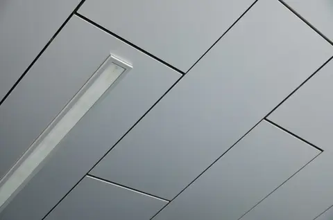 Suspended gray acoustic ceiling tiles arranged in a herringbone pattern with a white linear recessed light fixture running