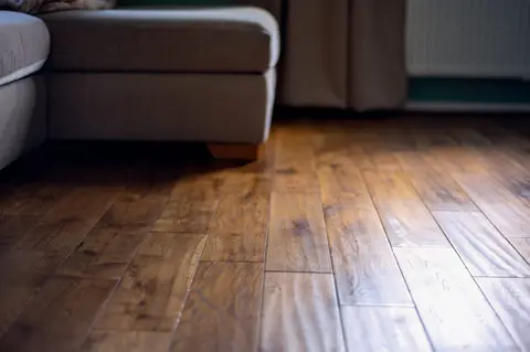 Warm-toned hardwood floor planks in a living room with gray upholstered furniture and baseboards.