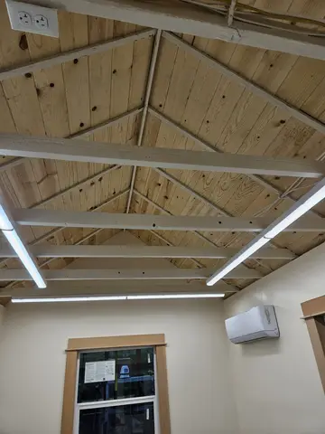 Vaulted wood beam ceiling with exposed framing, recessed LED light strips, and white ductless mini-split unit mounted on