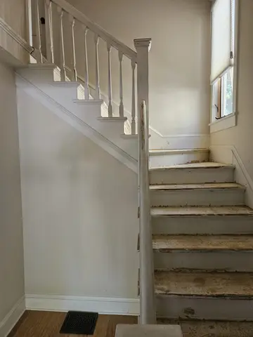 Interior staircase with white drywall wall panels, exposed wooden steps, metal spindle railing, and natural light from upper