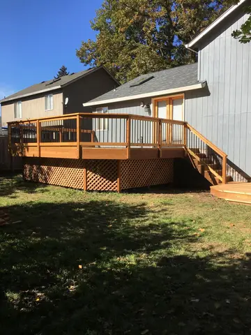 Multi-level wooden deck with tan railings, composite decking, and crosshatch lattice skirting attached to modern house with