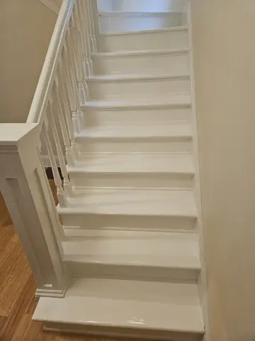 White painted wooden staircase descending with white balusters, handrail, and wood flooring visible at landing.