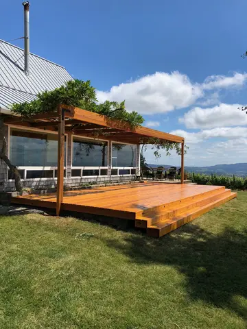 Newly built wooden deck with attached pergola, glass railings, and mountain vista beyond.
