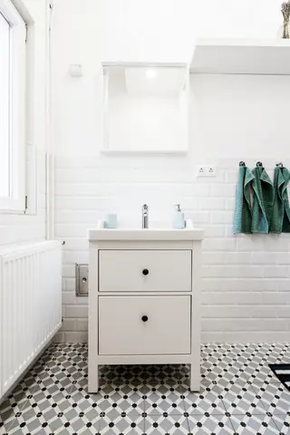 White wooden bathroom vanity with two black-knob drawers, white sink, and mirror above, set on black-and-white hexagonal