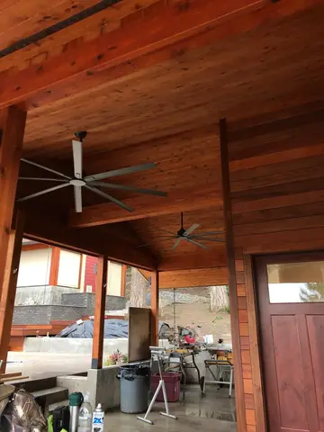 Covered patio interior with exposed wood beam ceiling, two ceiling fans, concrete floor, and red door visible on right.