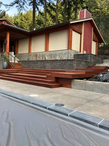 Modern home exterior with dark red vertical wood siding, cream stucco panels, horizontal mahogany-toned deck stairs