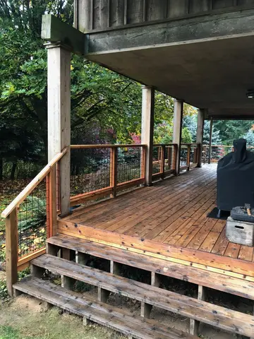 Wooden deck with composite boards, metal mesh railing, and concrete support structure overhead.