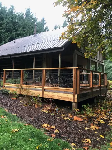 Black cabin with standing-seam metal roof and wooden deck featuring wire mesh railings and enclosure, surrounded by