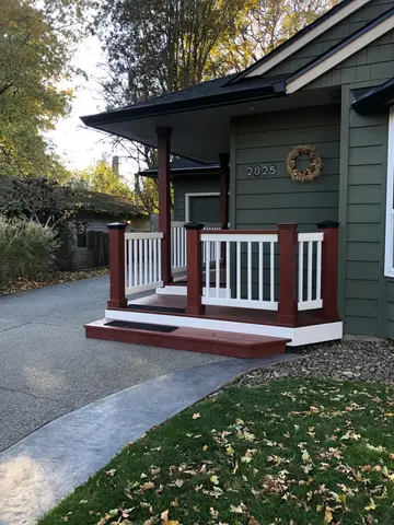 Front porch addition with dark green siding, red-painted deck base, white spindle railings, and covered entry overhang.