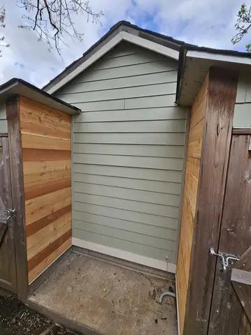 Garden shed with gray horizontal lap siding, gabled roof, and two wooden entry doors with hardware.