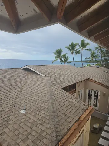 Completed asphalt shingle roof viewed from covered structure, ocean and palm trees in background.