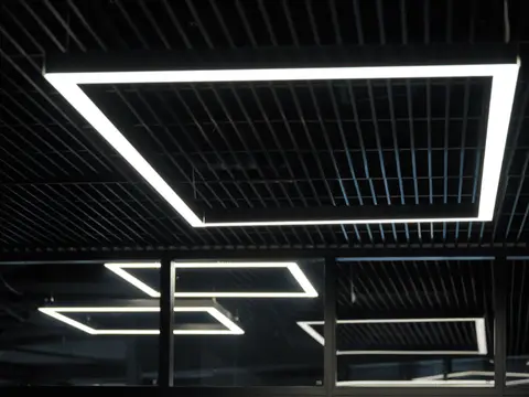 Modern recessed linear neon ceiling lights arranged in geometric rectangular pattern against dark slatted ceiling.