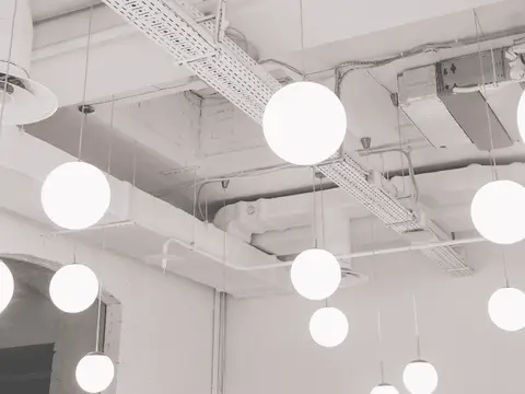 Multiple white globe pendant lights hang from a clean white ceiling with exposed metal ductwork and cable trays in a modern