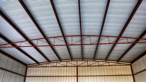 Interior view of industrial roof structure with exposed steel beams, corrugated polycarbonate panels, and metal framework.
