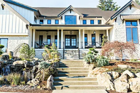 Modern farmhouse home with white columns, blue-shuttered upper story, stone and siding facade, covered front porch with