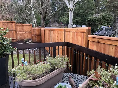 Multi-level wood deck with black metal railings, built-in curved planter boxes with greenery, and mature trees in background.