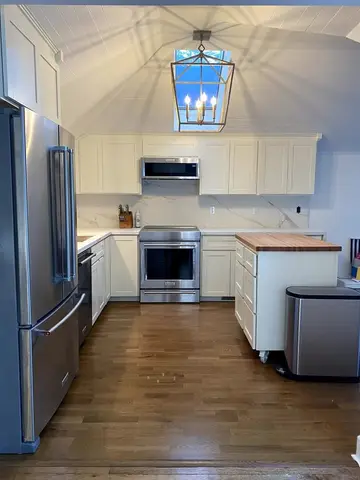 Modern kitchen with white shaker-style cabinetry, stainless steel refrigerator and range, wood countertop on island