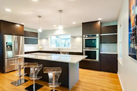 Modern kitchen with dark wood cabinetry, white quartz countertops, stainless steel appliances, center island with bar