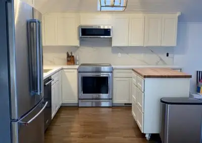 Modern kitchen with white shaker cabinetry, stainless steel refrigerator and range, marble backsplash, wood island
