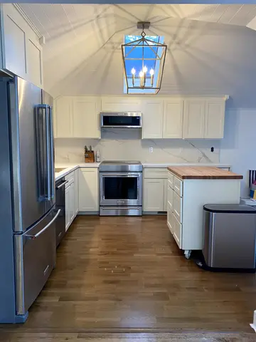 Modern kitchen featuring white shaker cabinetry, stainless steel refrigerator and range, wood countertop on island, hardwood