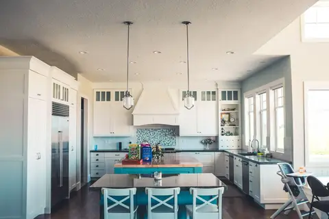 Modern kitchen with white upper and lower cabinetry, turquoise-painted island with cross-back stools, teal tile backsplash